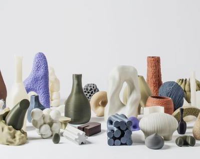 Különböző színű és formájú 3D nyomtatott tárgyak világos felületen: vázák, organikus formák és kisebb geometrikus darabok.